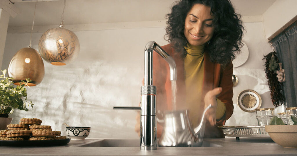 Kvinde bruger kogende vandhane til at fylde kedel med kogende vand